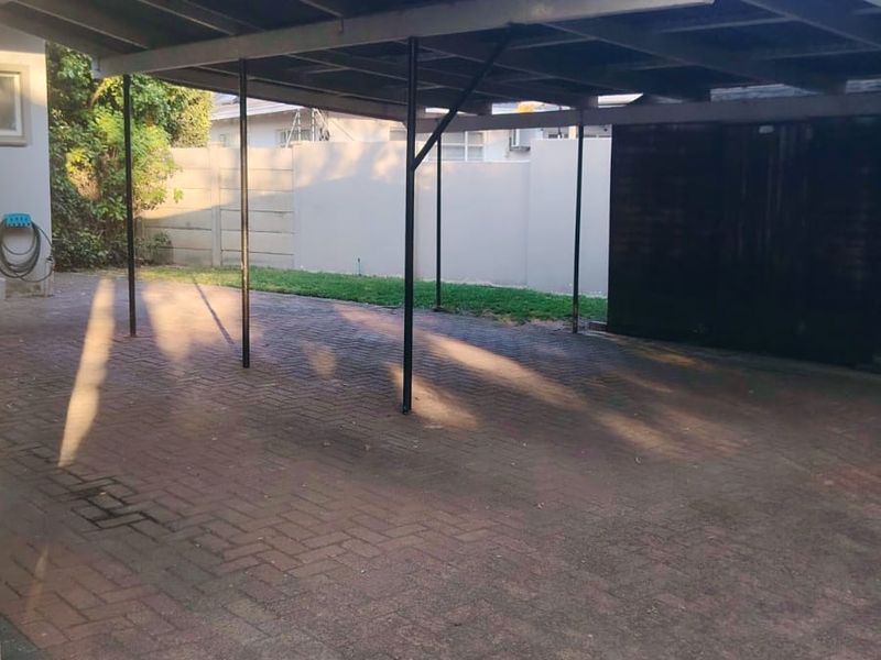 A spacious paved driveway featuring a large covered carport structure, providing ample off-street parking and secure vehicle storage.