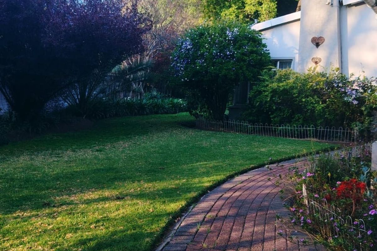 A well-maintained rear garden featuring a curved brick paved pathway, lush lawn, and established greenery alongside the house structure.