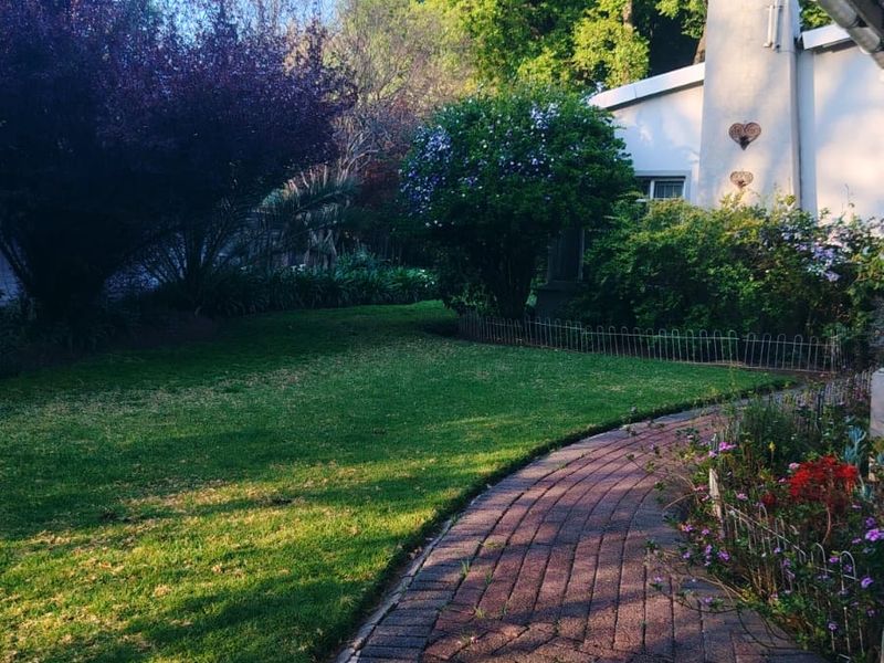 A well-maintained rear garden featuring a curved brick paved pathway, lush lawn, and established greenery alongside the house structure.