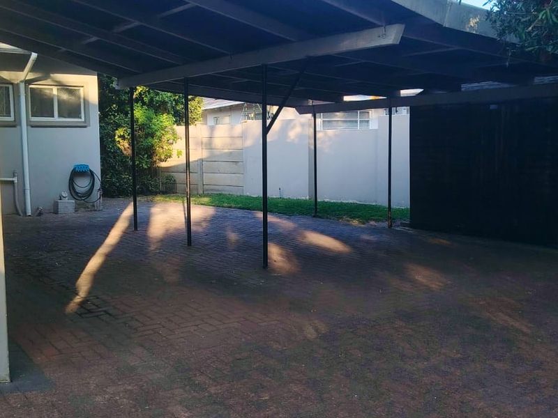 A functional outdoor carport area featuring a paved driveway and secure boundary walling, providing covered parking space.
