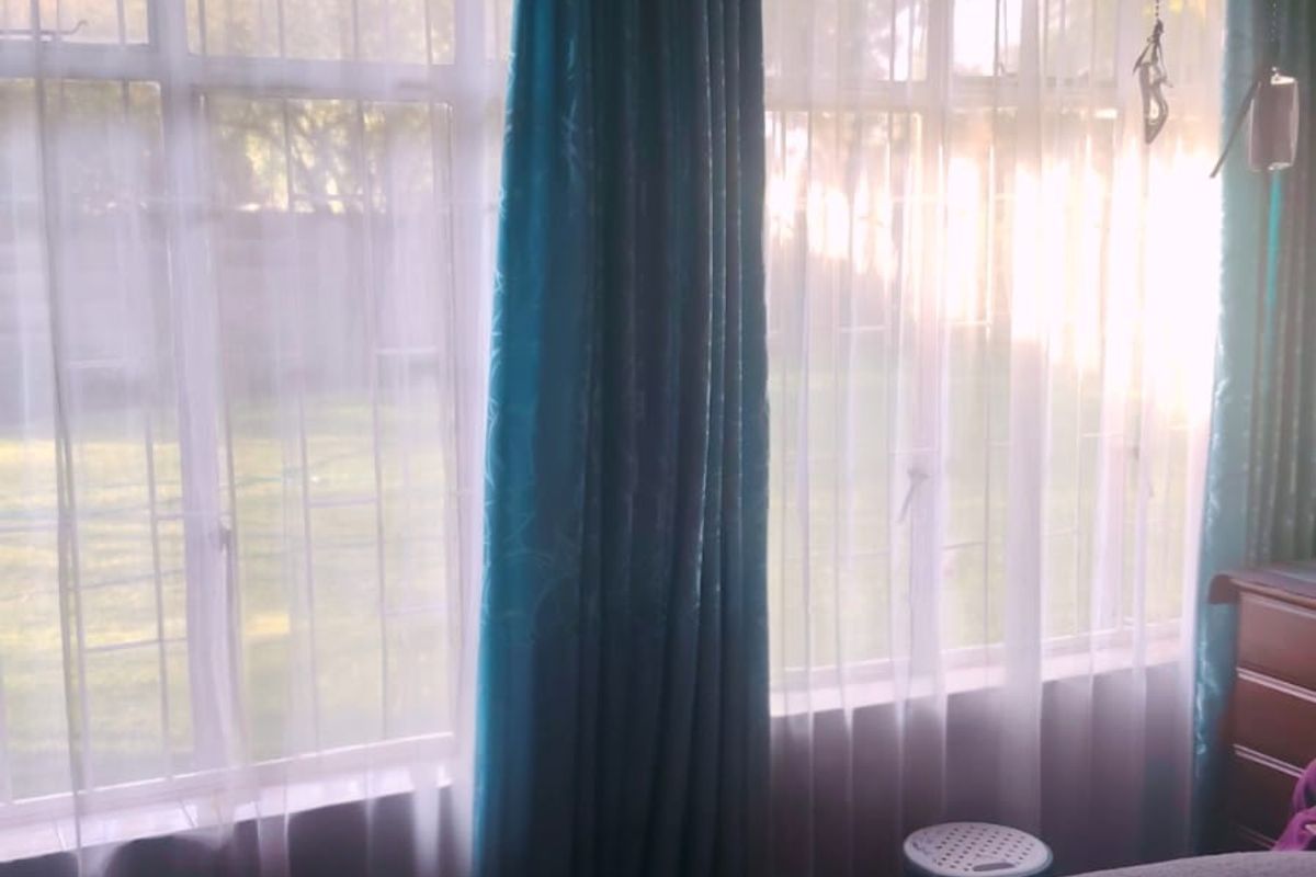 A bedroom featuring parquet flooring, a wall-mounted air conditioning unit, and large windows allowing natural light.