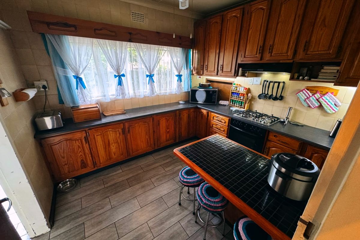 A functional kitchen featuring traditional wooden cabinetry, a gas hob with extractor fan, tiled backsplash, and a tiled breakfast counter.