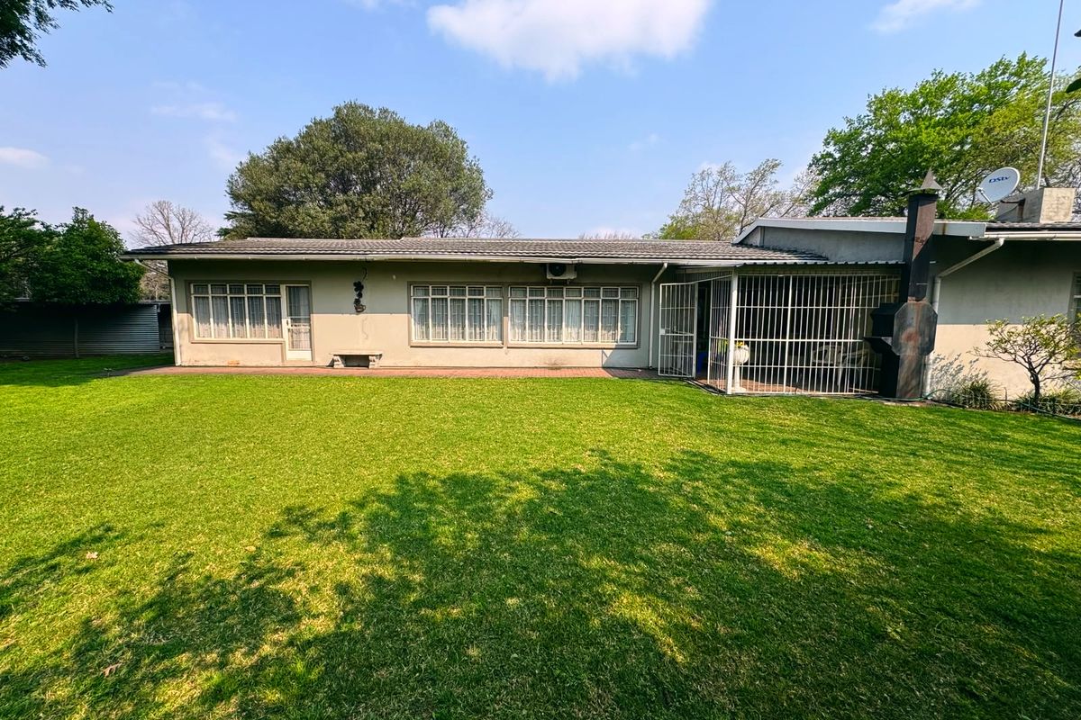 Rear view of the house featuring a spacious lawn, paved patio area, and an outdoor fireplace.