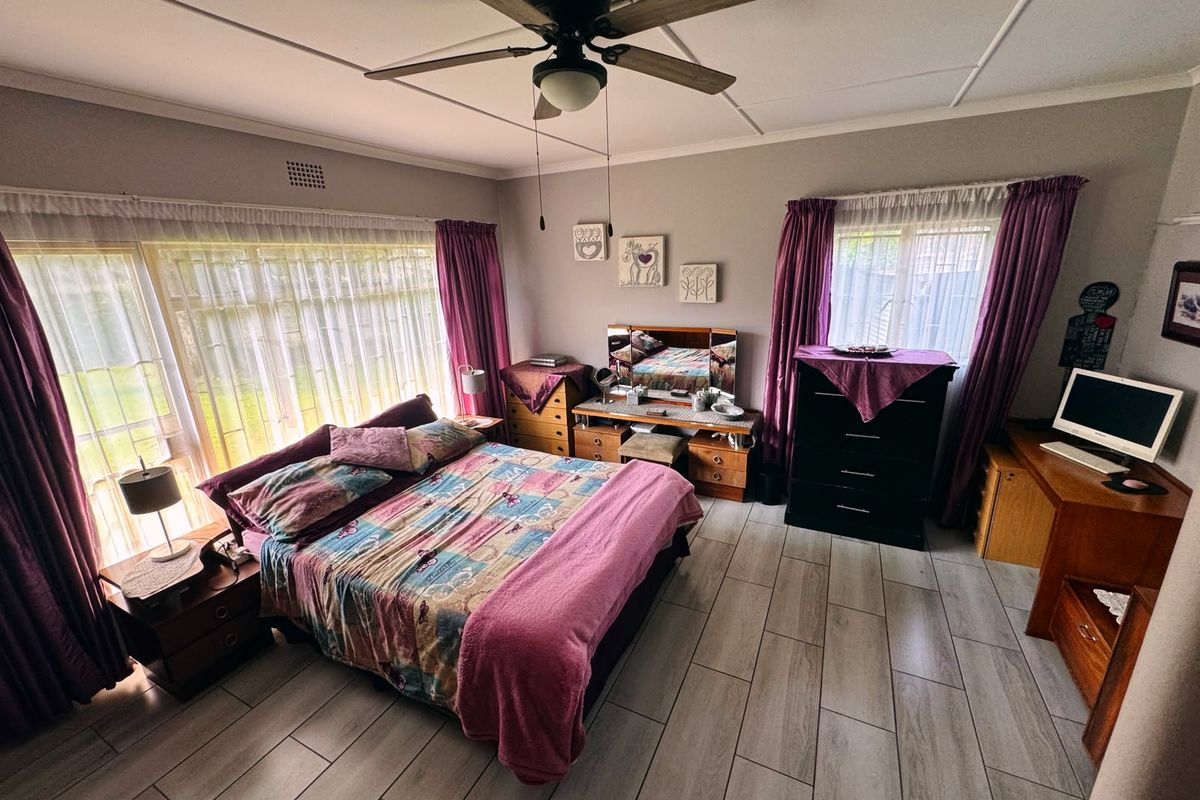A spacious bedroom featuring light-toned tiled flooring, a ceiling fan, and large windows that provide ample natural light.