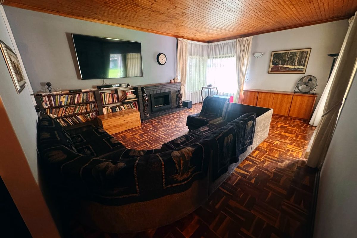 Spacious living room featuring classic parquet flooring, a timber-clad ceiling, and a central brick fireplace with integrated shelving.