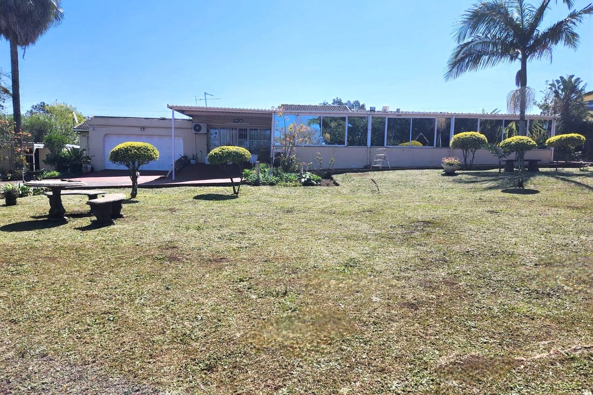 Rear view of the property featuring an enclosed patio, attached garage, and a spacious landscaped garden with mature palm trees.