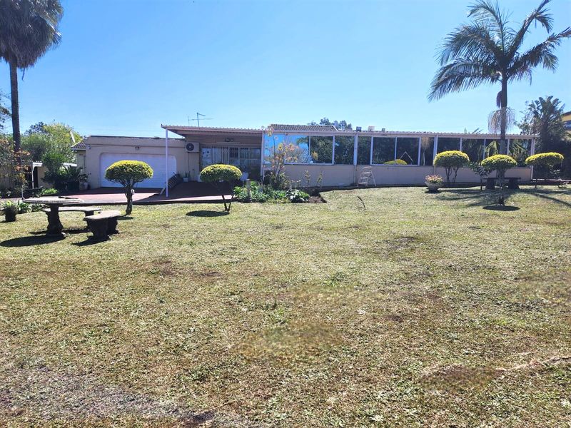 Rear view of the property featuring an enclosed patio, attached garage, and a spacious landscaped garden with mature palm trees.