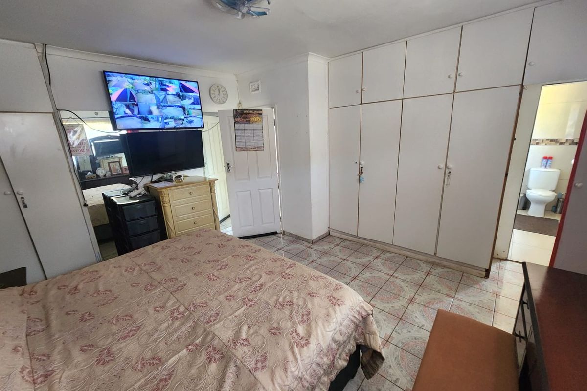 Bedroom featuring built-in cupboards, tiled flooring, and an en-suite bathroom, offering a functional layout with potential for cosmetic updates.