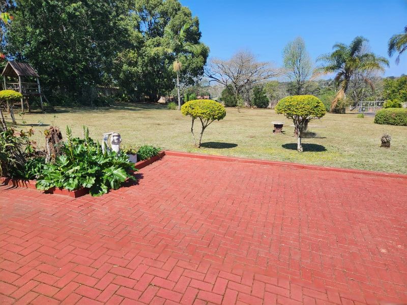 A spacious backyard featuring a red brick paved patio area overlooking a large, well-established garden with mature trees and lawn.