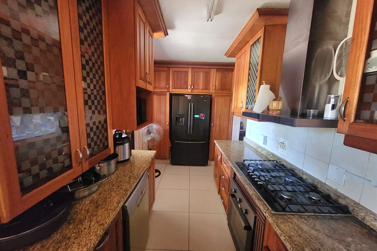 A galley-style kitchen featuring wooden cabinetry, granite countertops, a built-in oven, gas hob, and extractor fan with tiled flooring.