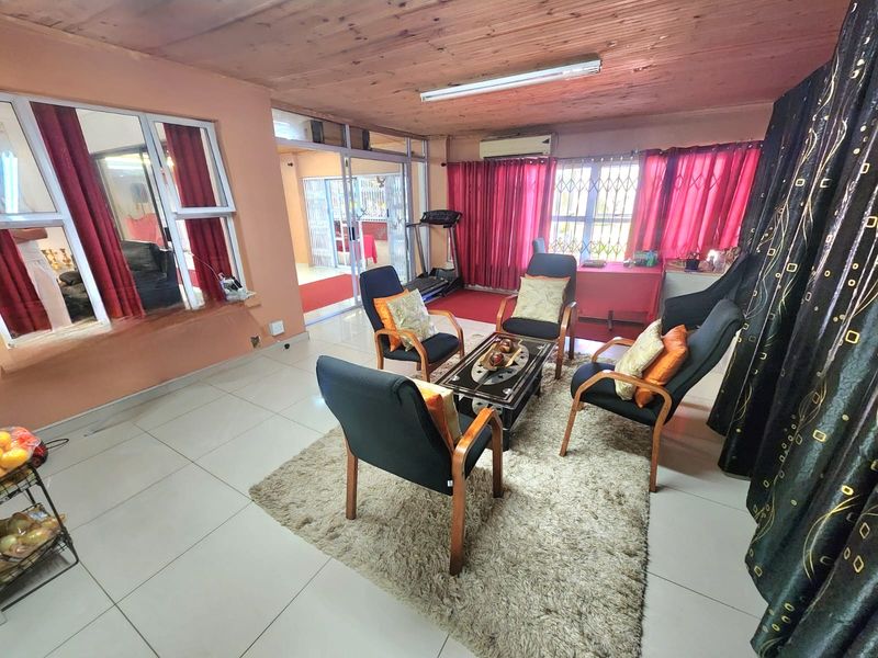 Spacious living area featuring tiled flooring, timber ceiling, and large windows with security gates, providing access to an adjacent room through sliding glass doors.