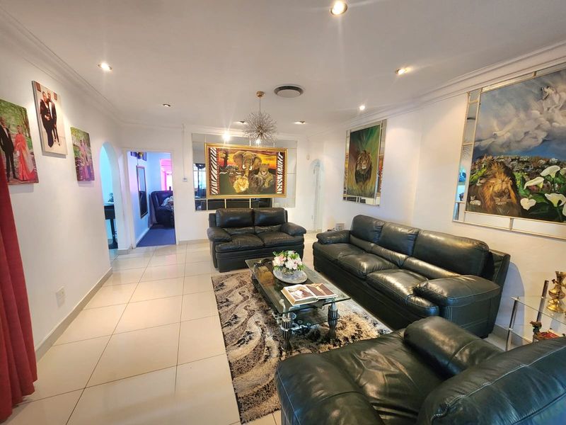 A spacious living room featuring tiled flooring, recessed downlighting, and decorative mirrored wall panels, creating a bright and well-maintained living area.