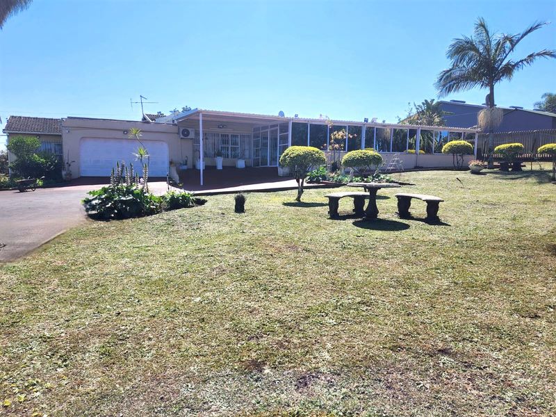 Rear view of the property featuring a large lawn, paved driveway, garage, and a spacious covered patio area.