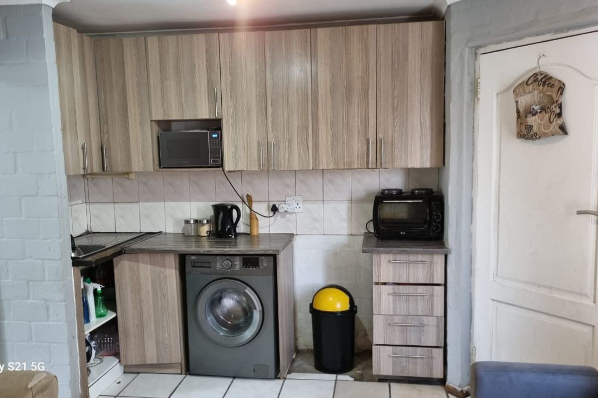 Compact kitchen featuring wood-look cabinetry, tiled backsplash, built-in microwave, and integrated washing machine space.