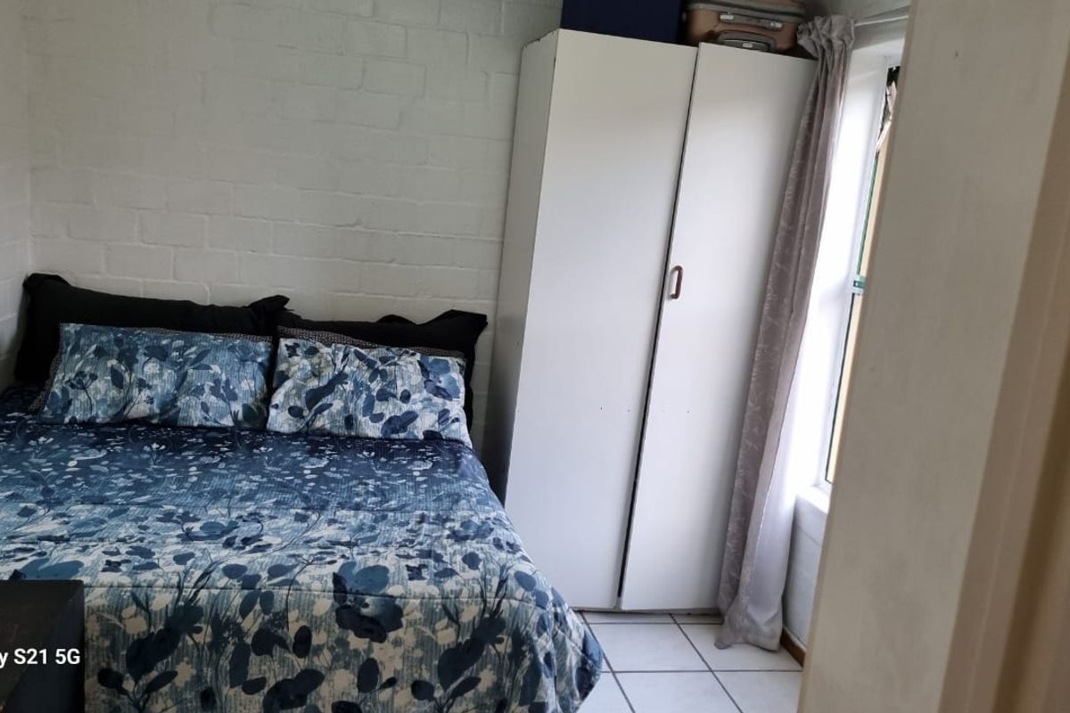 A bedroom featuring a built-in wardrobe, tiled flooring, and a painted brick wall, providing a functional living space.