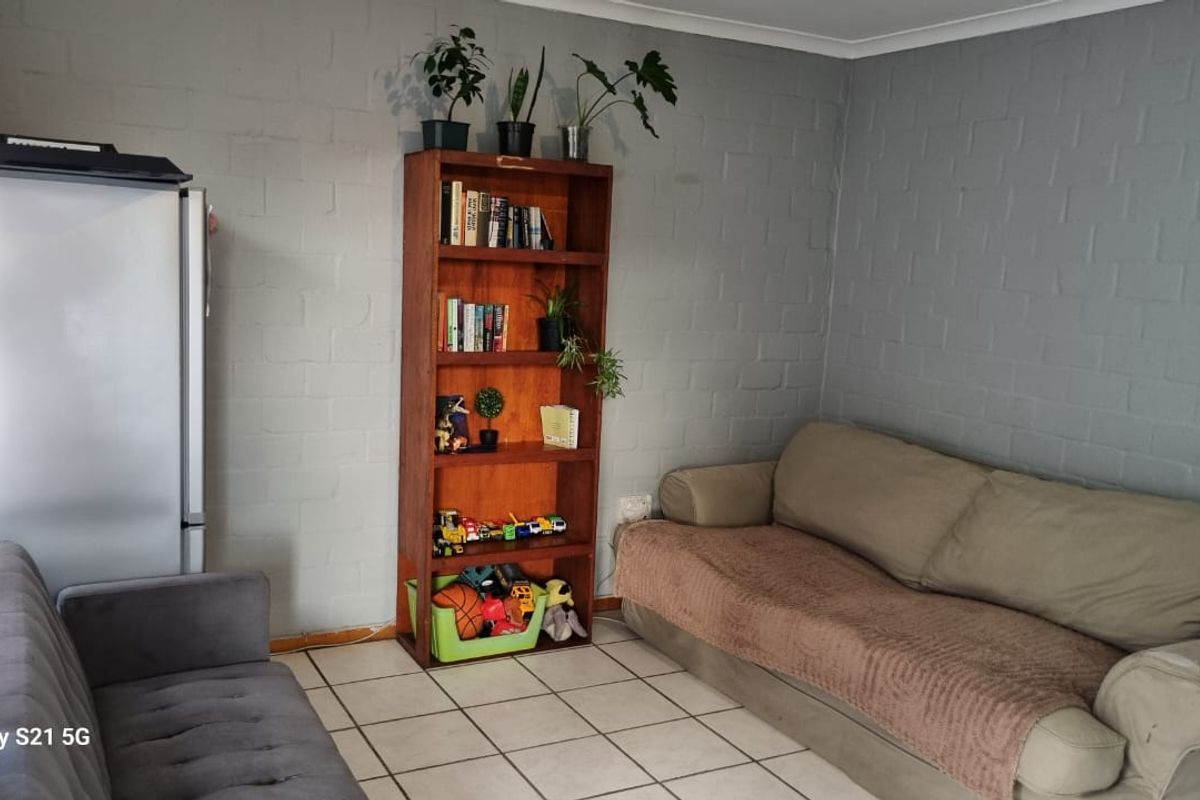A living room area featuring neutral tiled flooring and painted brick walls, providing a functional and versatile space.
