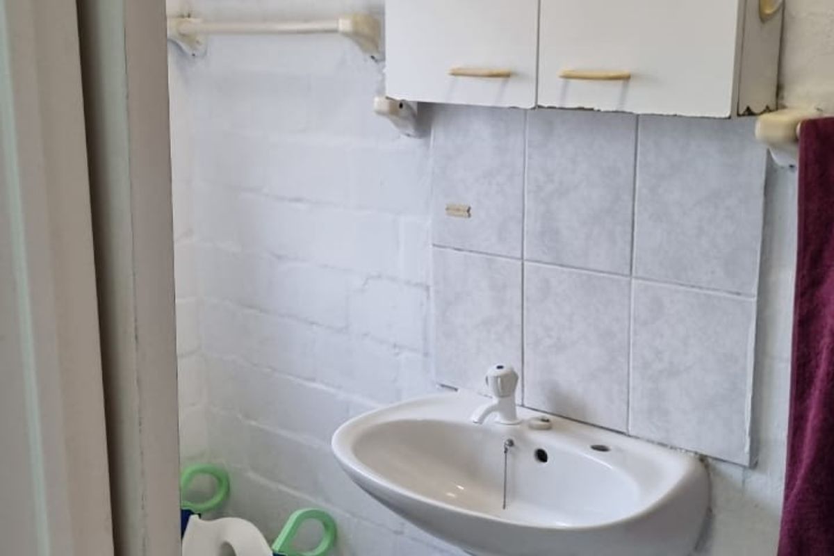 A compact bathroom featuring a wall-mounted basin, tiled splashback, and a white medicine cabinet, requiring cosmetic updates to improve the overall finish.