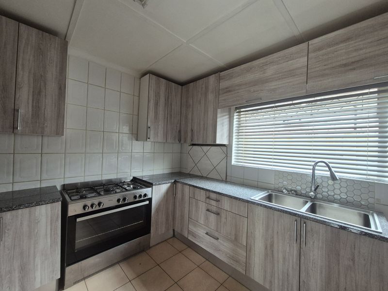A functional kitchen featuring wood-look laminate cabinetry, granite countertops, a gas stove with oven, and a double basin sink with tiled backsplash.