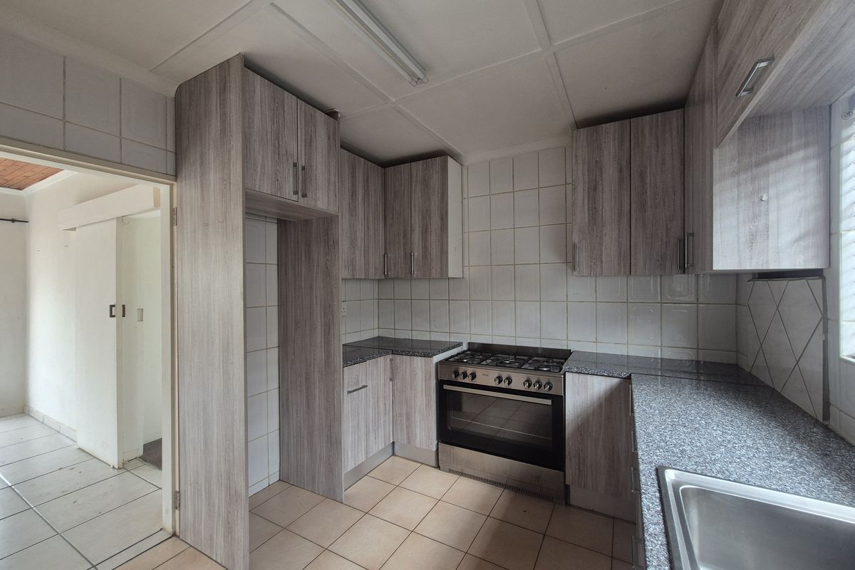 A functional kitchen featuring wood-look cabinetry, granite-effect countertops, a gas stove, and tiled finishes, offering a clean space ready for personalization.
