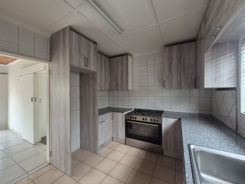 A functional kitchen featuring wood-look cabinetry, granite-effect countertops, a gas stove, and tiled finishes, offering a clean space ready for personalization.