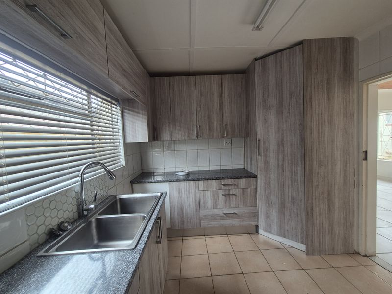A clean and functional kitchen featuring modern wood-look laminate cabinetry, granite countertops, a double stainless steel sink, and neutral ceramic floor tiling.