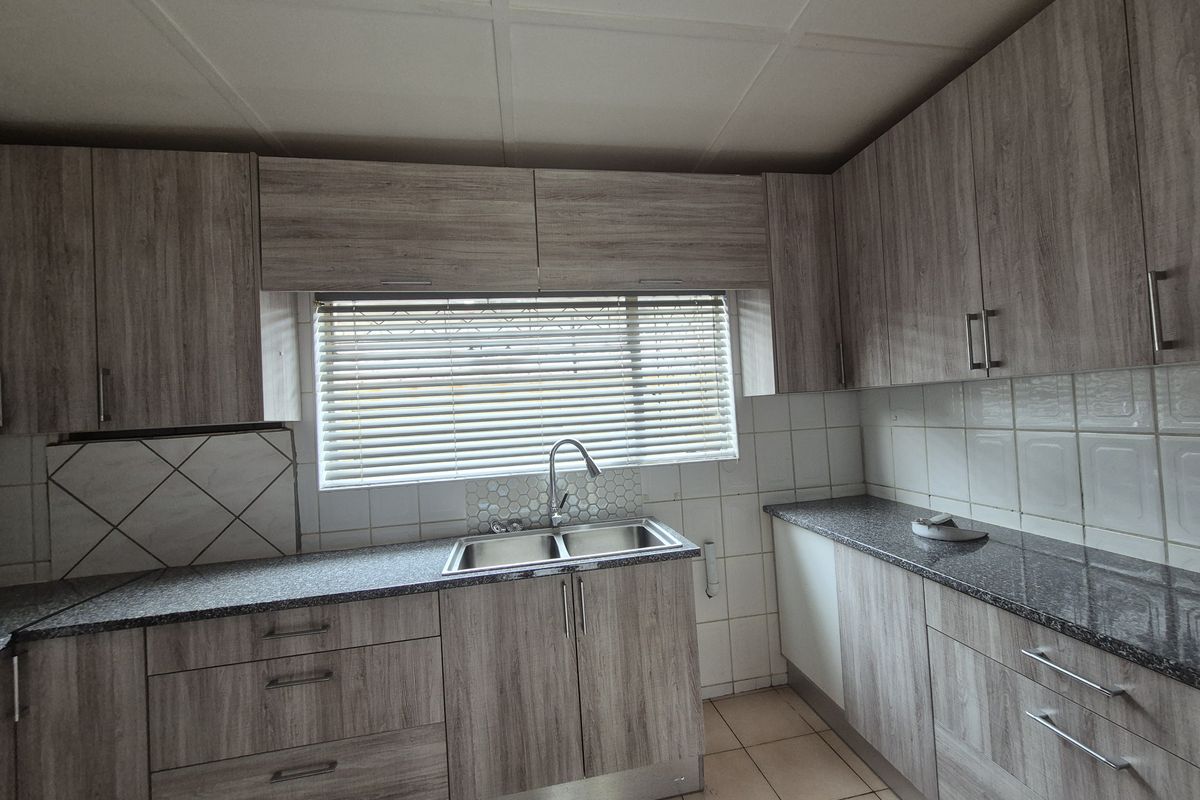 A functional kitchen featuring wood-look laminate cabinetry, granite countertops, a double basin sink, and tiled backsplash with neutral ceramic flooring.