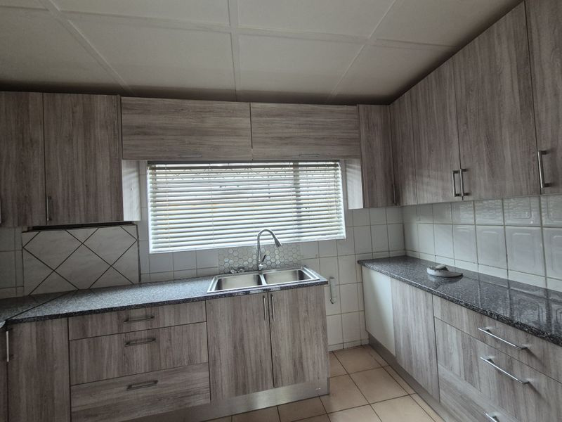 A functional kitchen featuring wood-look laminate cabinetry, granite countertops, a double basin sink, and tiled backsplash with neutral ceramic flooring.