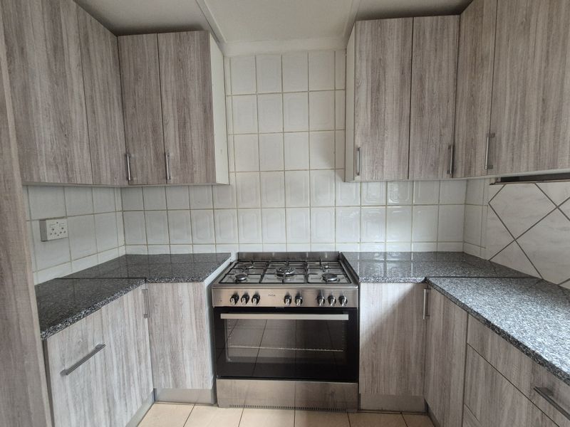 A functional kitchen featuring wood-look cabinetry, granite countertops, a gas stove with oven, and a clean tiled backsplash.