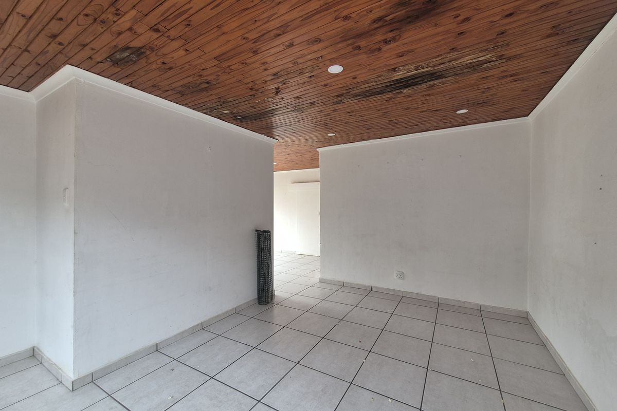 An empty living area featuring ceramic floor tiles and a timber tongue and groove ceiling with visible signs of water damage.