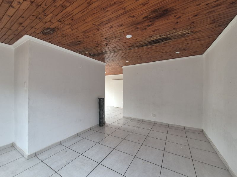 An empty living area featuring ceramic floor tiles and a timber tongue and groove ceiling with visible signs of water damage.