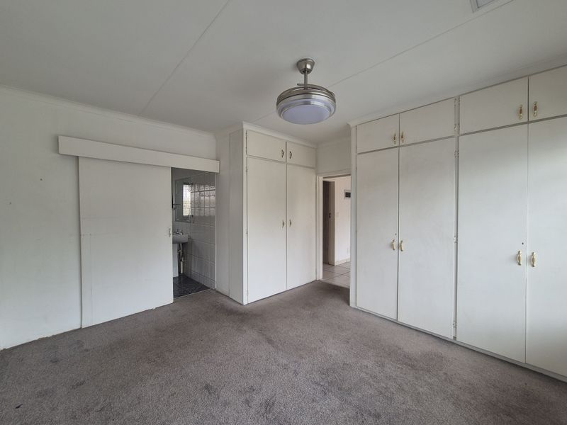 A spacious bedroom featuring extensive built-in cupboards, a ceiling fan, and direct access to an en-suite bathroom area.
