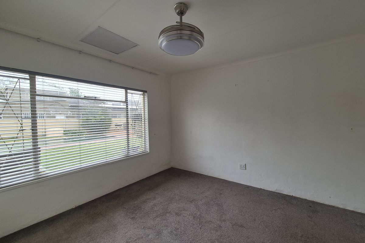 An empty bedroom featuring a ceiling fan, carpeted flooring, and large windows with venetian blinds, offering a blank canvas for renovation.