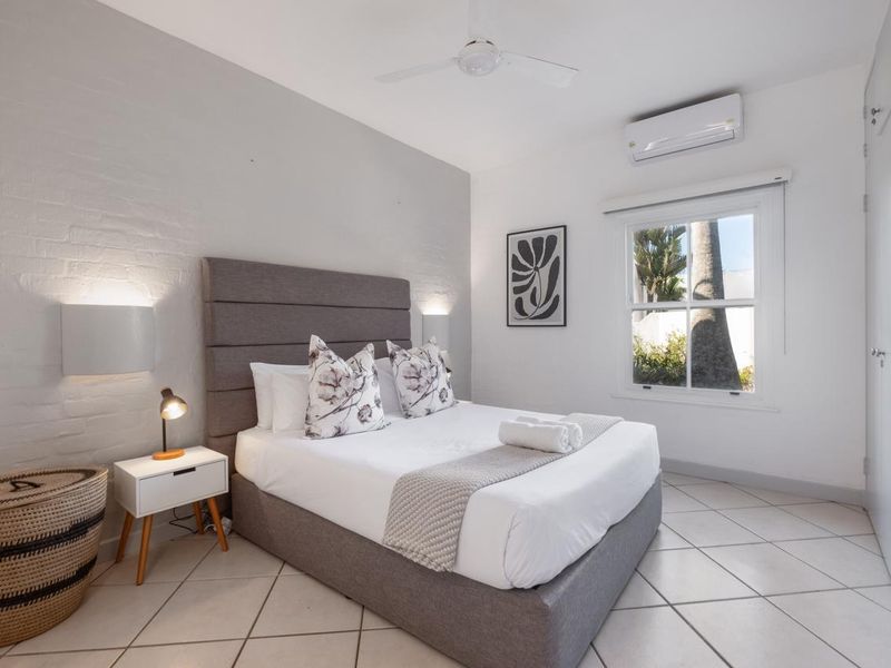 A well-maintained bedroom featuring tiled flooring, a painted brick feature wall, built-in cupboards, a ceiling fan, and a split-system air conditioner.