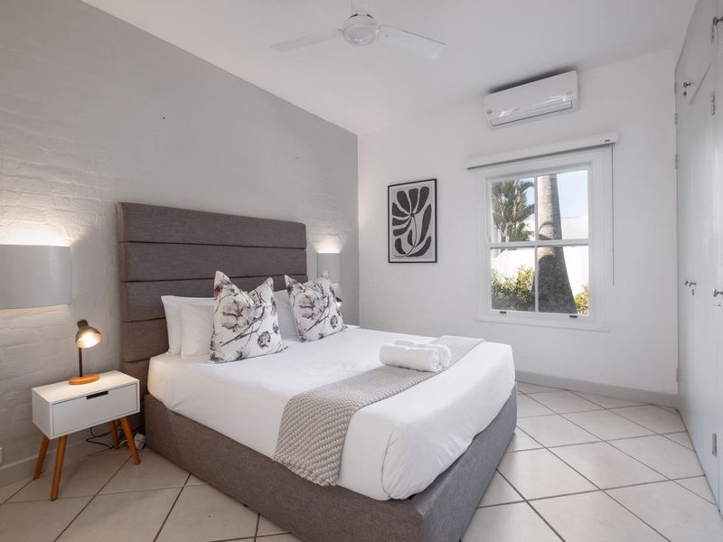 A bright, well-maintained bedroom featuring tiled flooring, a built-in wardrobe, a ceiling fan, and a split-system air conditioning unit.