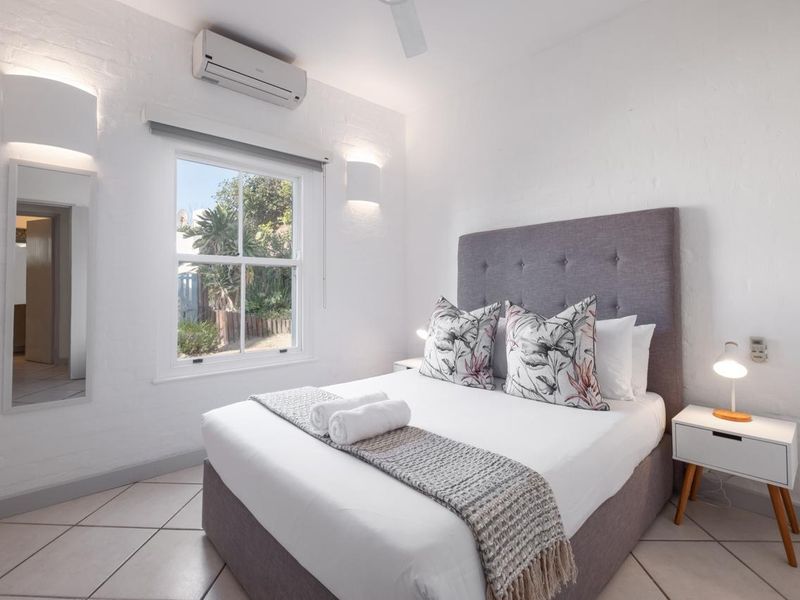 A bright and well-maintained bedroom featuring tiled flooring, a split-system air conditioner, ceiling fan, and wall-mounted lighting.