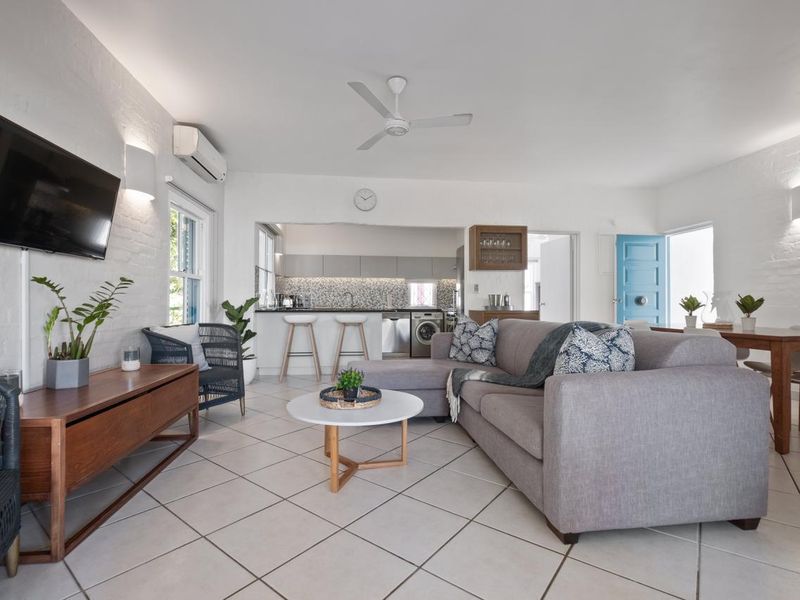 Bright open-plan living and dining area featuring tiled floors, exposed brick walls, and a modern kitchen with integrated appliances and breakfast bar.