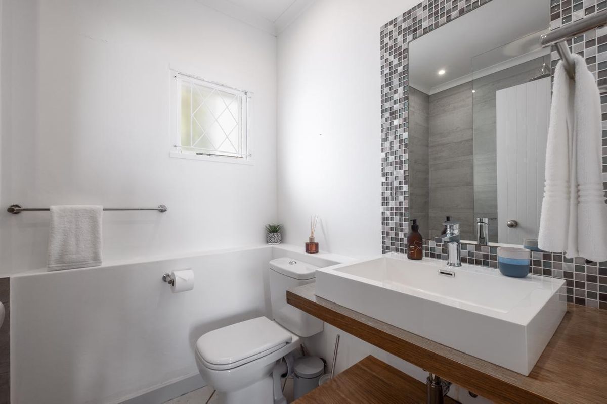 A modern bathroom featuring a vessel sink on a wooden vanity, mosaic tile accents, and a wall-mounted mirror.