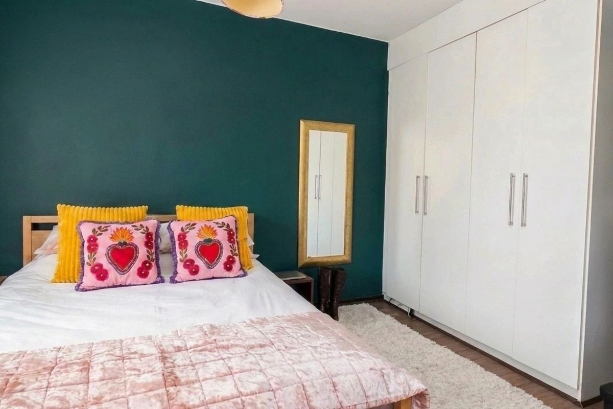 A well-maintained bedroom featuring a deep green accent wall and ample built-in wardrobe storage.