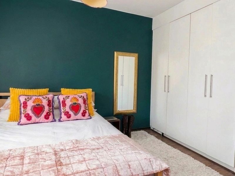 A well-maintained bedroom featuring a deep green accent wall and ample built-in wardrobe storage.