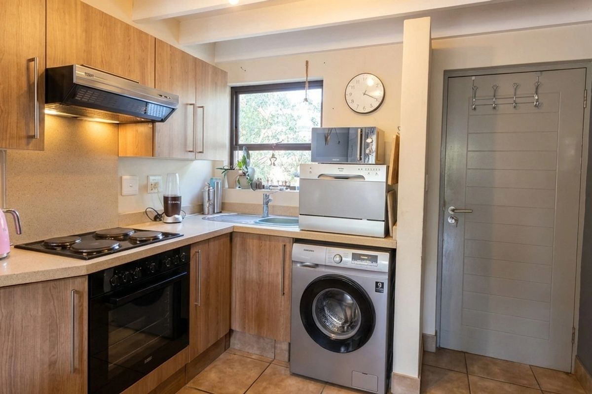 Compact kitchen featuring wood-finish cabinetry, integrated appliances, electric hob, oven, and tiled flooring with exposed ceiling beams.