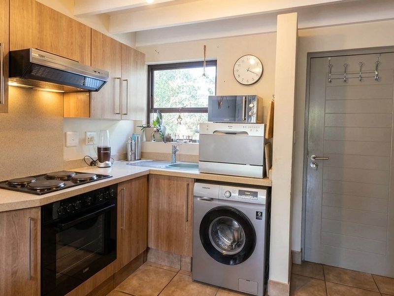 Compact kitchen featuring wood-finish cabinetry, integrated appliances, electric hob, oven, and tiled flooring with exposed ceiling beams.