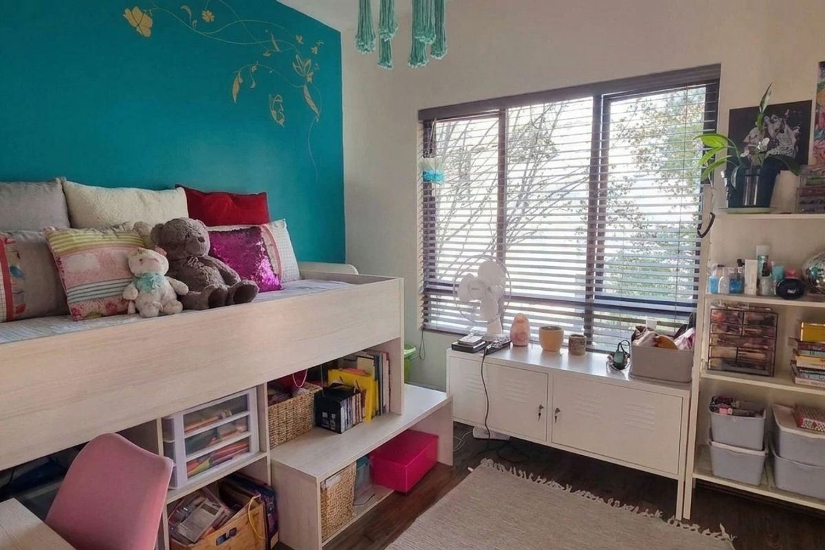 A bedroom featuring laminate flooring and venetian blinds, with a bold accent wall and functional layout.