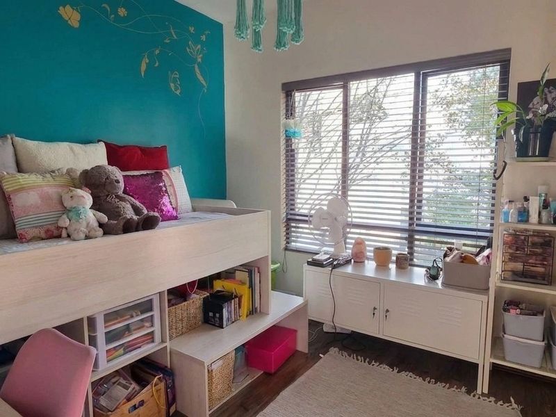 A bedroom featuring laminate flooring and venetian blinds, with a bold accent wall and functional layout.