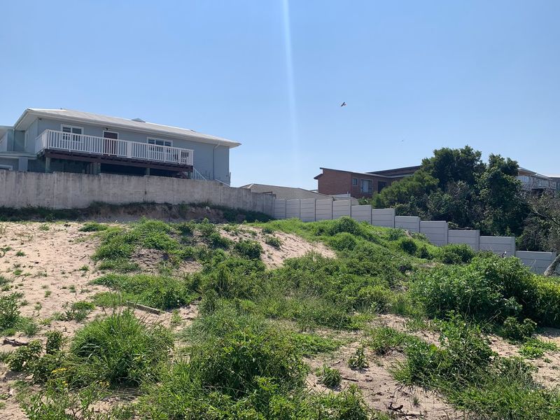A view of a vacant residential plot featuring a sandy slope, retaining wall, and precast concrete boundary fencing adjacent to existing residential properties.