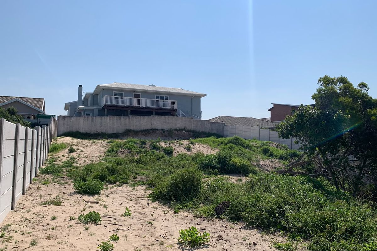 A view of a vacant residential plot featuring sandy terrain, coastal vegetation, and a precast concrete boundary wall with an adjacent property visible.