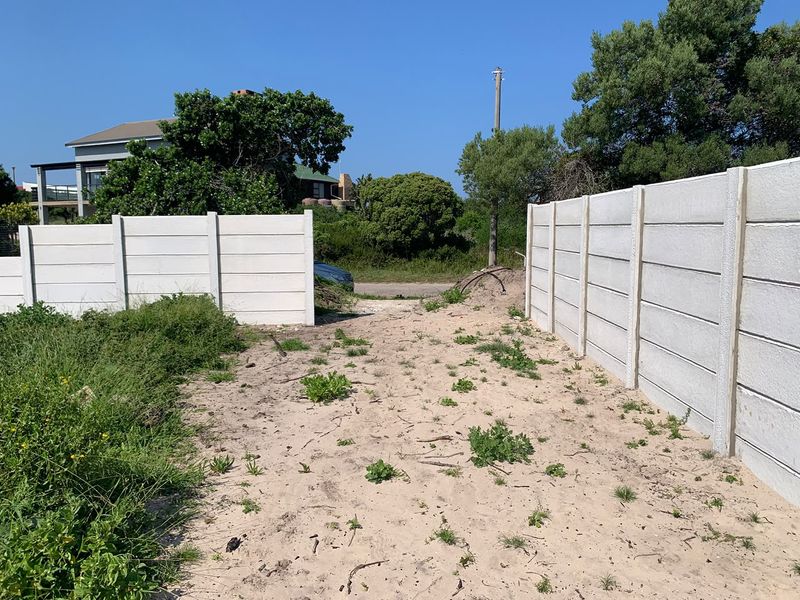 A view of the vacant residential plot entrance, featuring precast concrete boundary walls and an unpaved sandy access path.