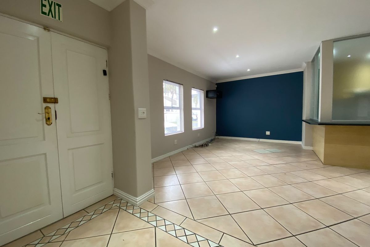 An empty, open-plan living area featuring tiled floors, recessed lighting, a built-in counter, and a double door entrance with an exit sign.