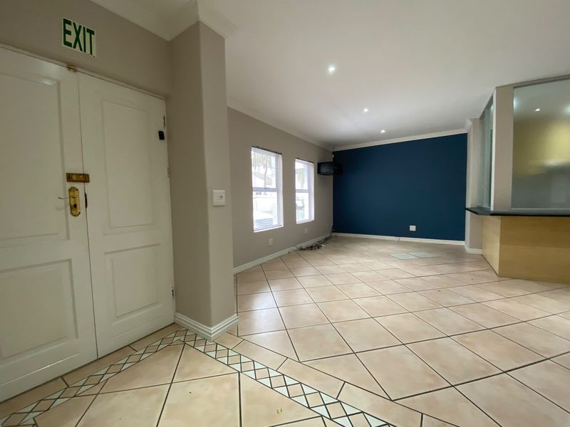 An empty, open-plan living area featuring tiled floors, recessed lighting, a built-in counter, and a double door entrance with an exit sign.