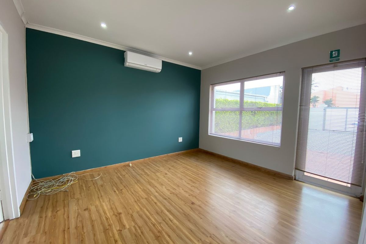 A bright, empty bedroom featuring laminate flooring, a split-system air conditioner, and large windows with fitted blinds.
