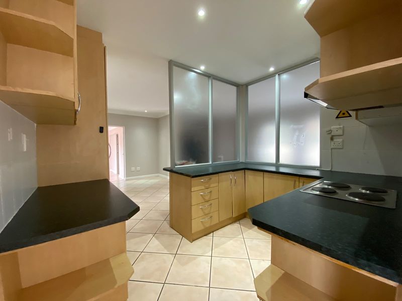 A functional kitchen featuring light wood cabinetry, dark laminate countertops, an integrated electric hob, and tiled flooring with an open-plan layout.